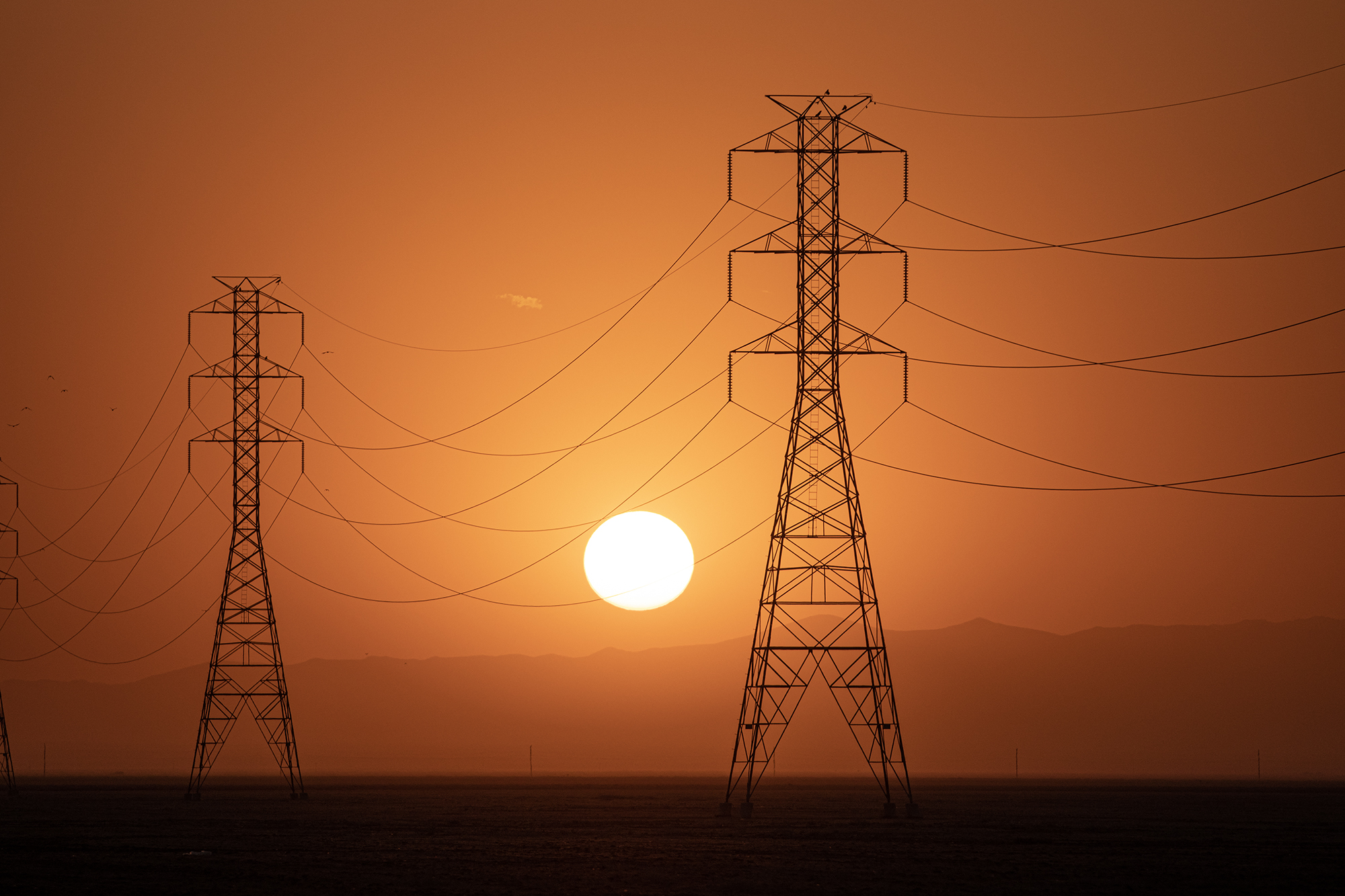 The sun sets behind a row of electrical towers in Fresno County on Sept. 6, 2022. Photo by Larry Valenzuela, CalMatters/CatchLight Local