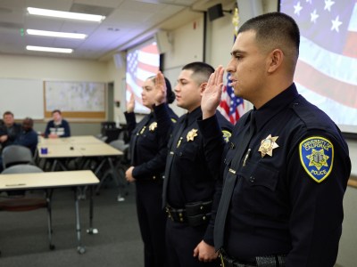 At right, UC Davis police officer Ernesto Moron repeats an oath along with fellow officers David Barilles and Daniella Flores at their swearing-in ceremony at the UC Davis Police department on Dec. 22, 2023. Photo by Fred Greaves for CalMatters